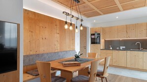 A modern kitchen with wooden cabinets, a built-in oven, and a dining area with a wooden table and chairs. - Apartment 'Sunset' with Mountain View, Private Terrace and Wi-Fi (St. Lorenzen)