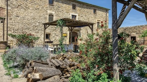 A stone building with a wooden pergola, a rustic outdoor seating area, and a pile of firewood. - Bed and Breakfast 'Fonolleres' with Shared Pool, Wi-Fi and Air Conditioning (Serra de Daró)