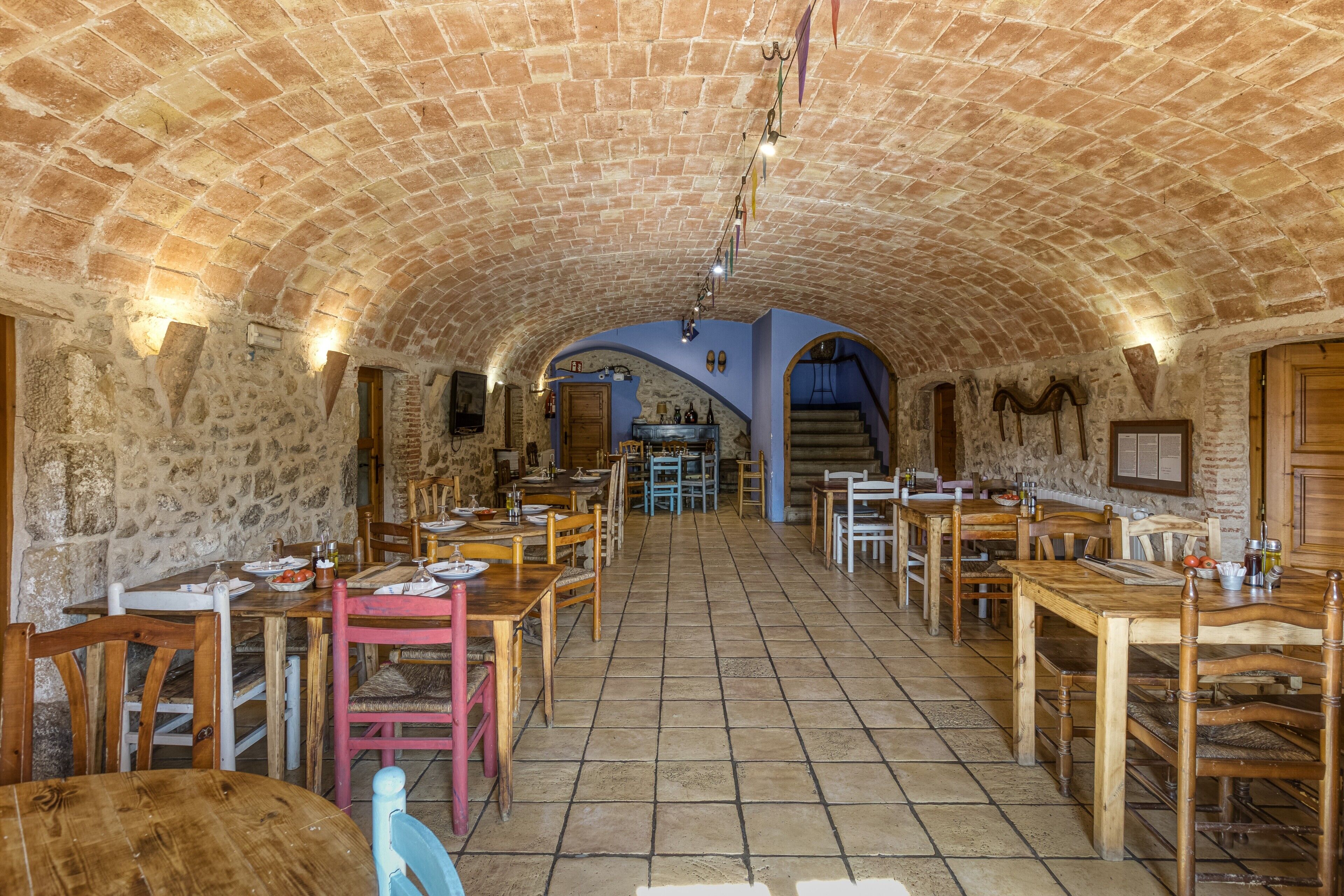 An interior with a brick ceiling, stone walls, wooden tables, and chairs arranged for dining.