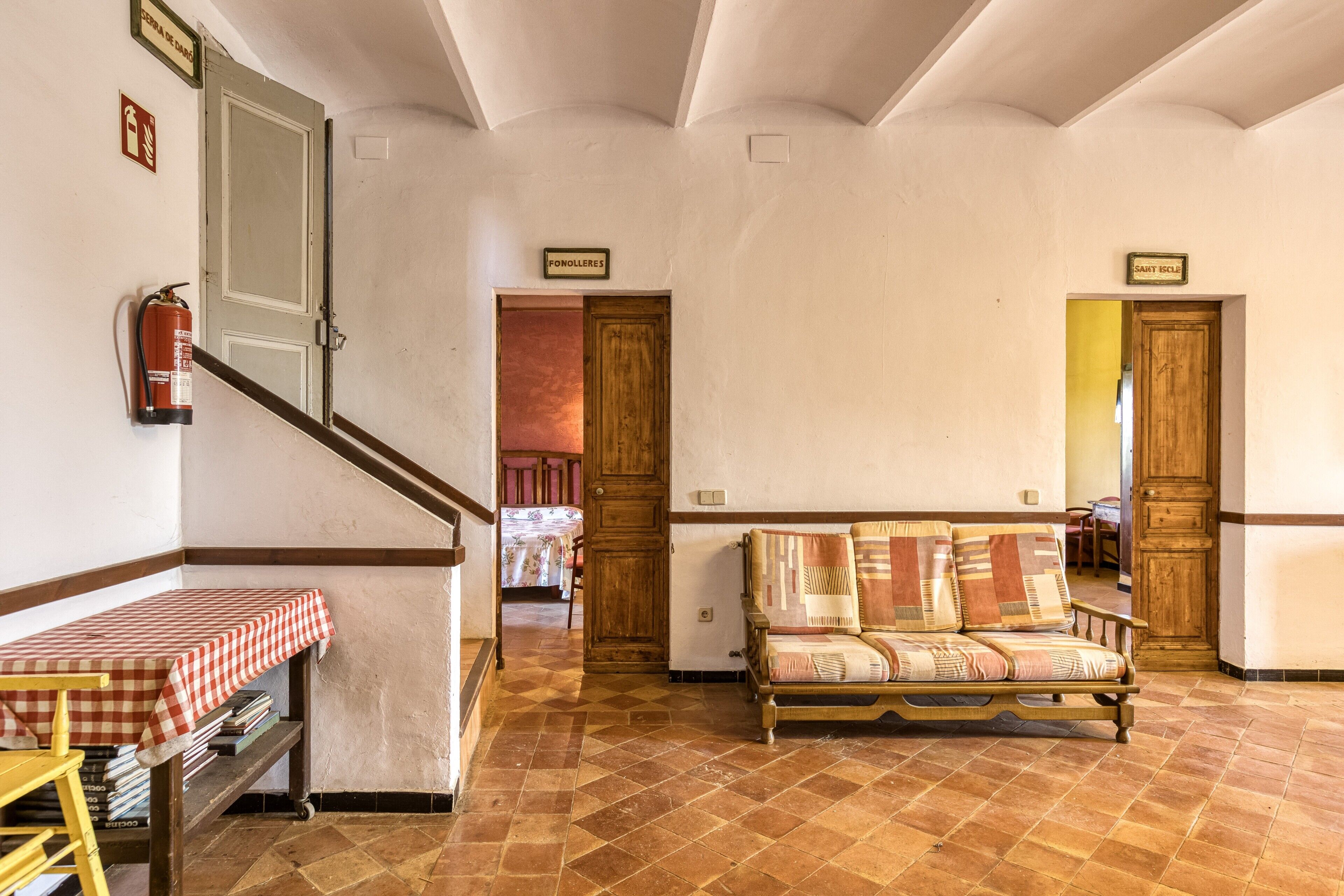 Una habitación con una mesa a cuadros, un sofá, una escalera de madera y un extintor.