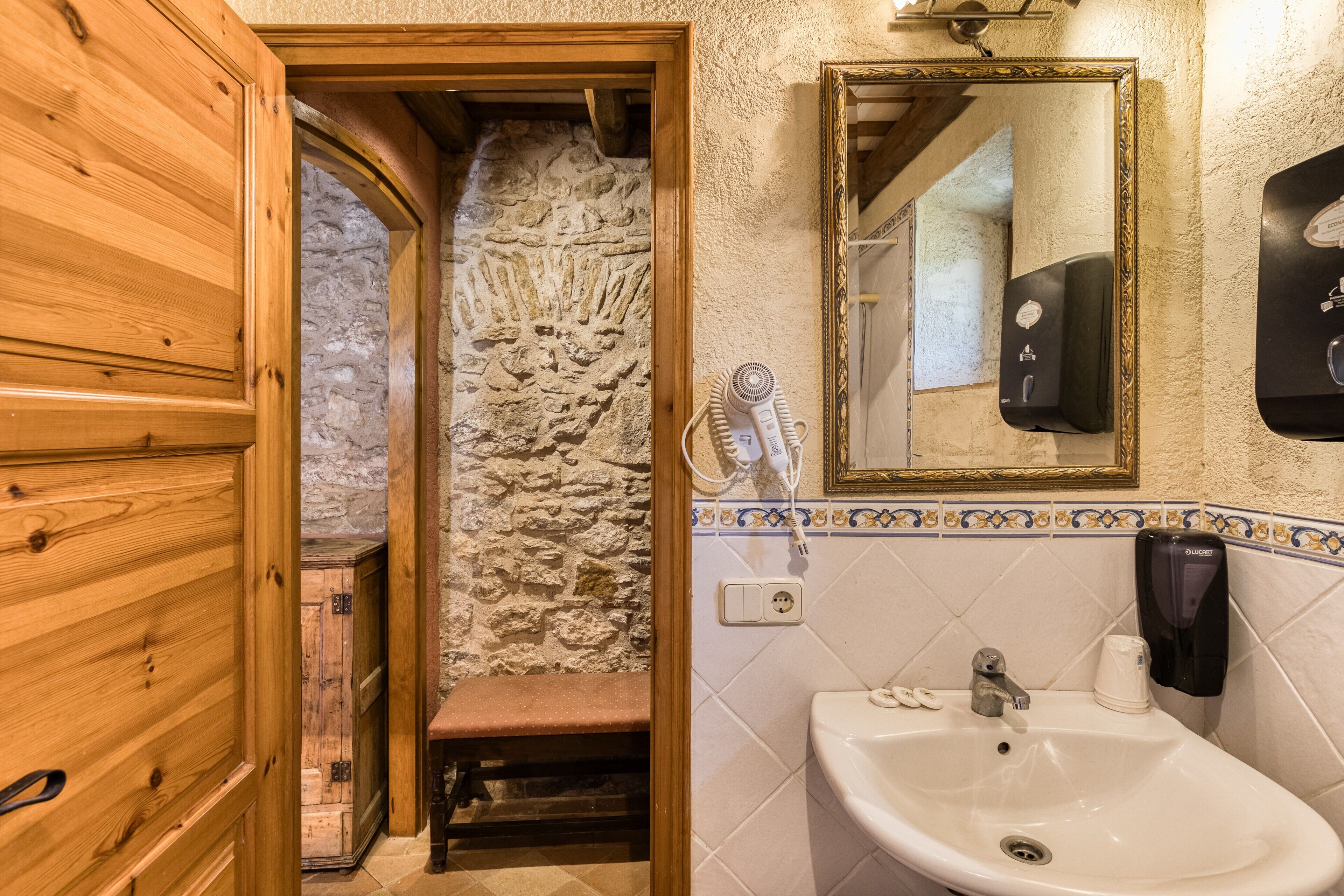 Une salle de bain avec une porte en bois, un mur en pierre, un lavabo avec un miroir et un sèche-cheveux.