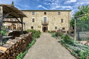 A stone building with a central entrance, a covered outdoor seating area, and a gravel path leading to the entrance. - Bed and Breakfast 'Estrella' with Shared Pool, Shared Terrace and Shared Garden (Serra de Daró)