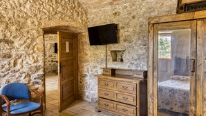 Habitación con paredes de piedra, un aparador de madera, un televisor montado en la pared y una cama con colcha estampada.