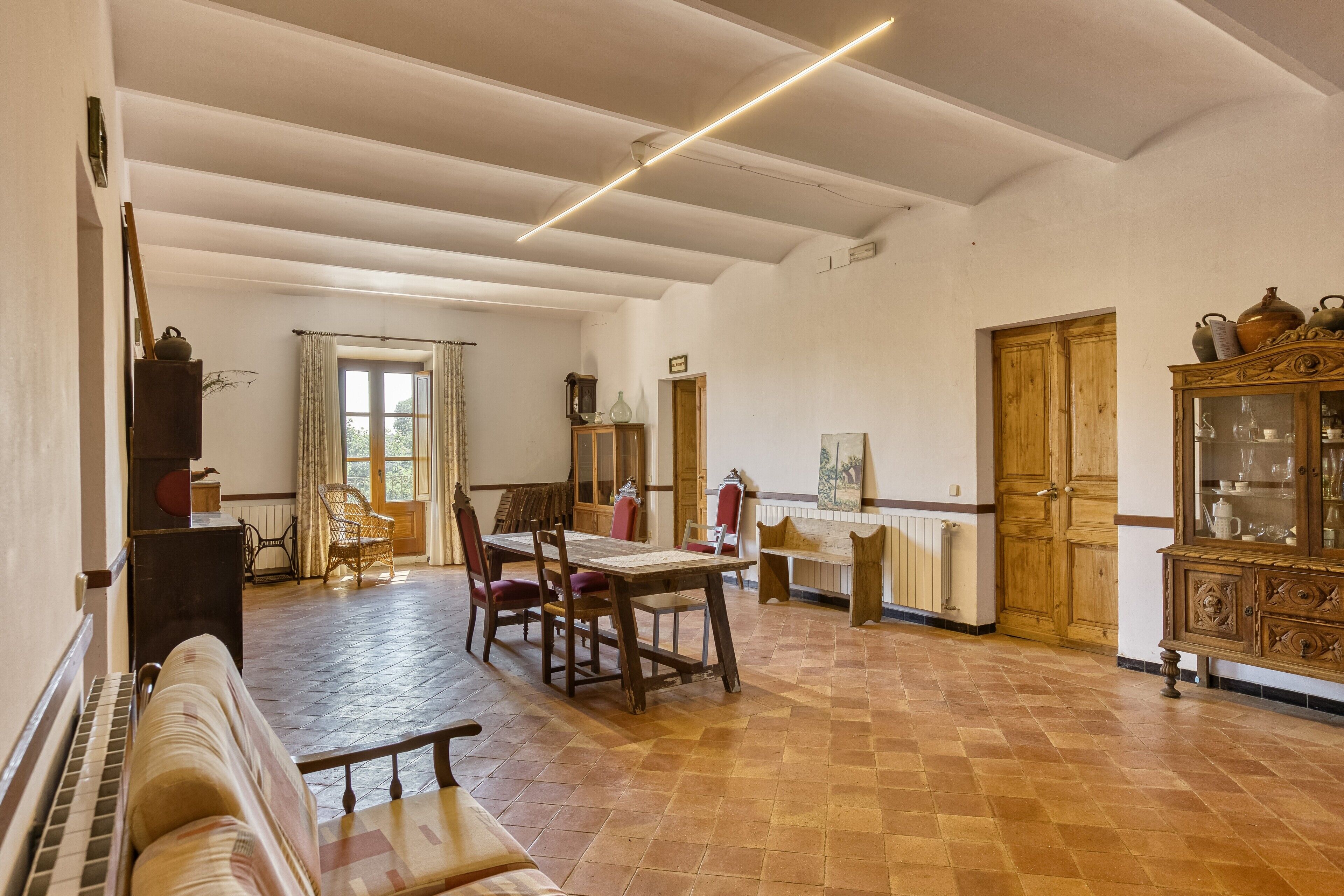 A spacious room with a wooden dining table, chairs, a piano, and a cabinet.