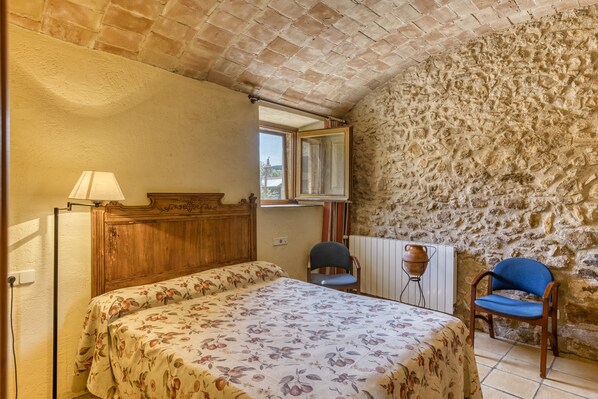 A bedroom with a bed, two chairs, a wooden cabinet, a stone wall, and a window. - Bed and Breakfast 'Estrella' with Shared Pool, Shared Terrace and Shared Garden (Serra de Daró)