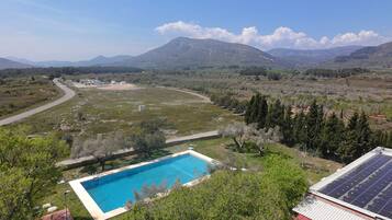 Una piscina envoltada de verdor, un camí sinuós i muntanyes a la distància.