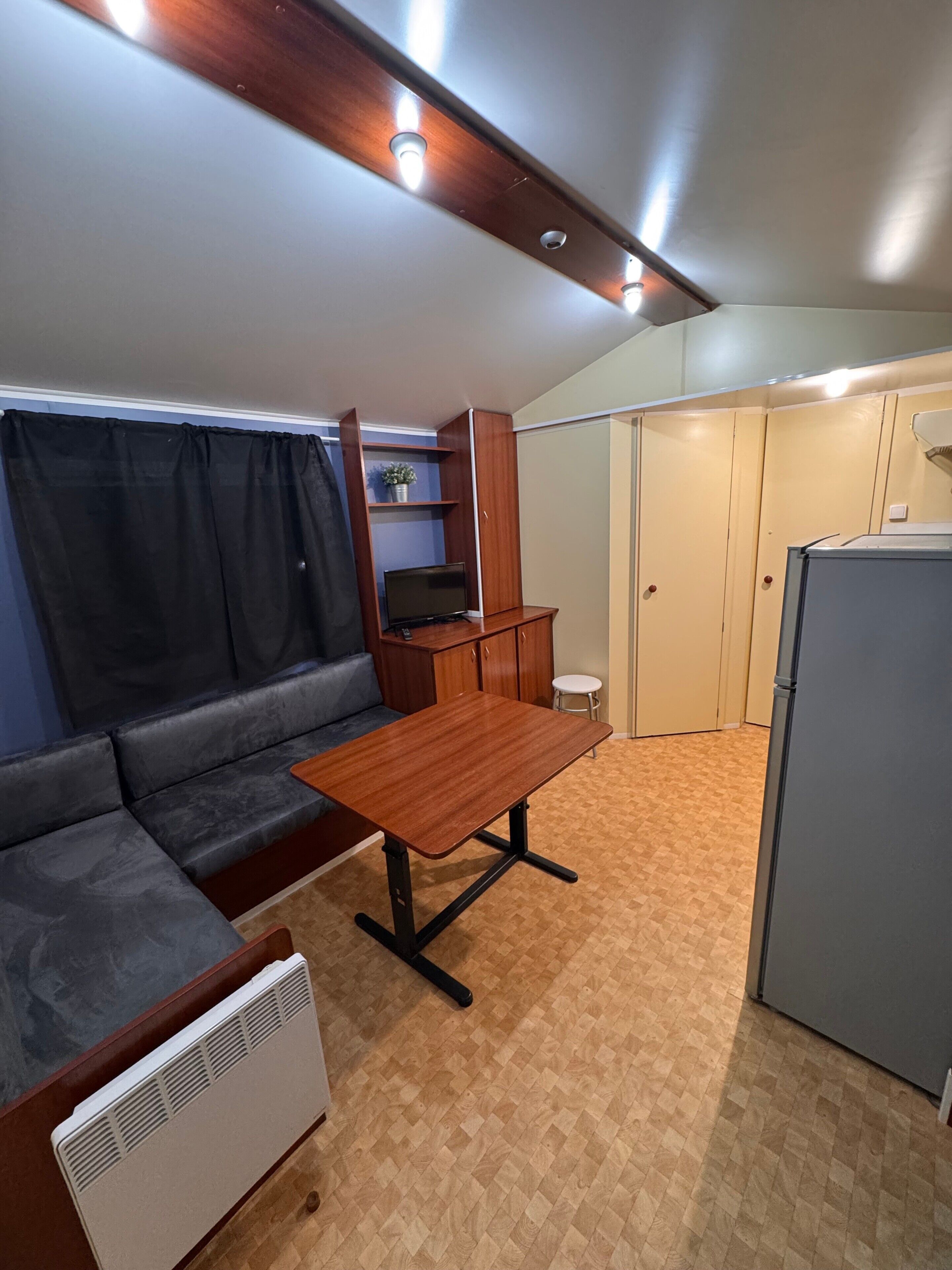 Un espace de vie compact comprenant un canapé, une table, un petit tabouret, un réfrigérateur et un meuble avec un téléviseur.