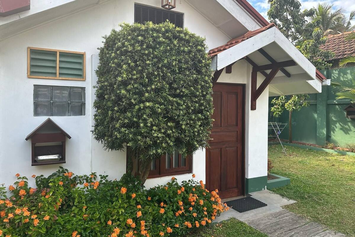 Uma casa com fachada branca, porta marrom e pequeno alpendre com estrutura de vigas de madeira.
