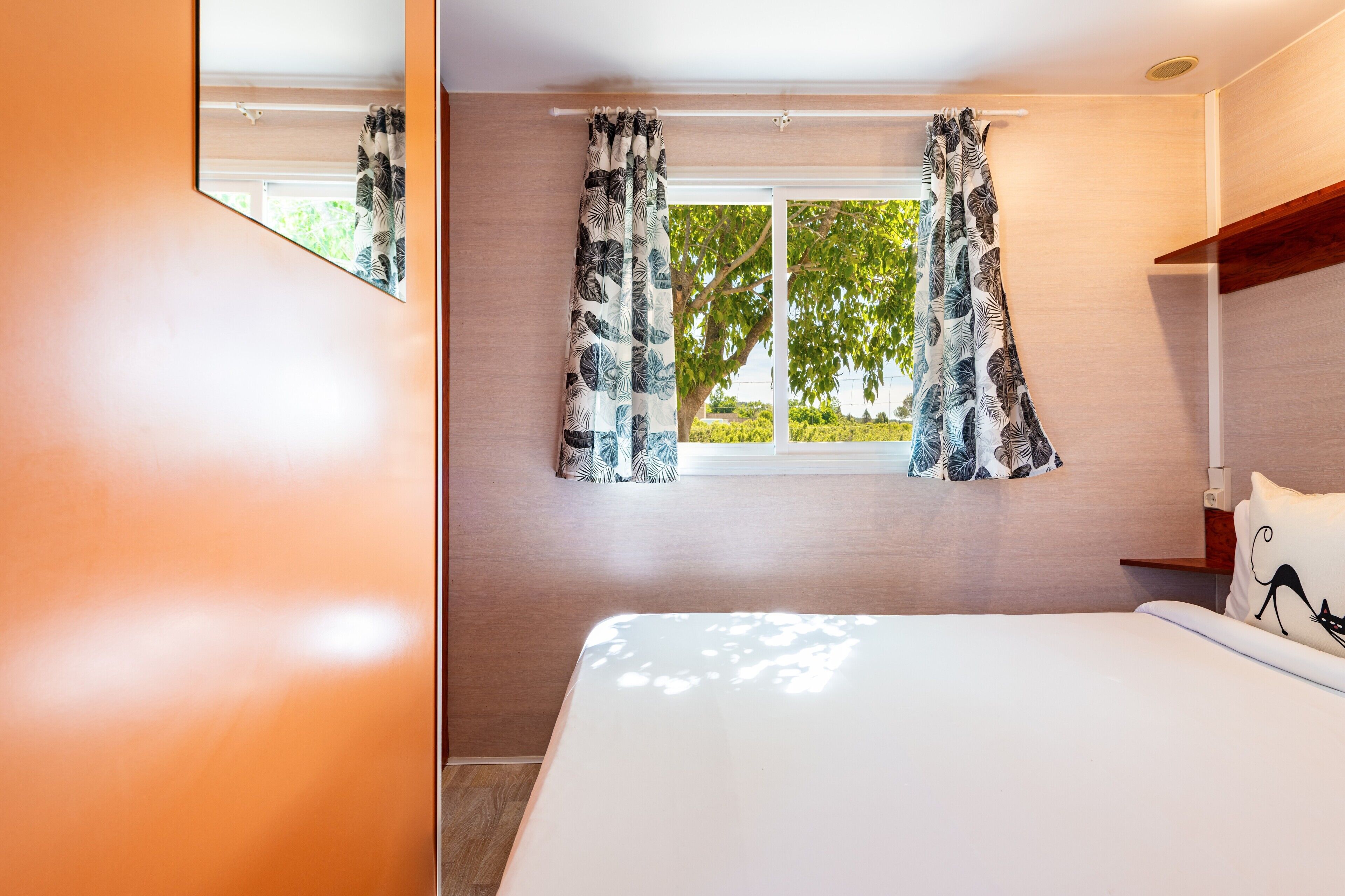 Una camera da letto con un letto, una finestra con tende, uno specchio e una mensola in legno.
