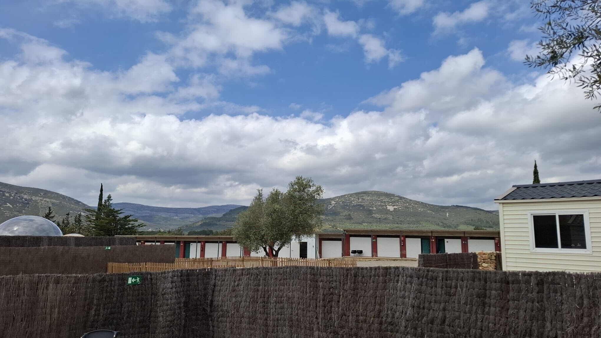 A row of cabins with a mountain backdrop, a clear sky, and a fence in the foreground.