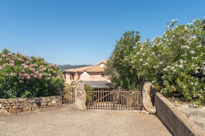 A gated entrance with a stone wall, a wooden gate, and a building with a tiled roof in the background.