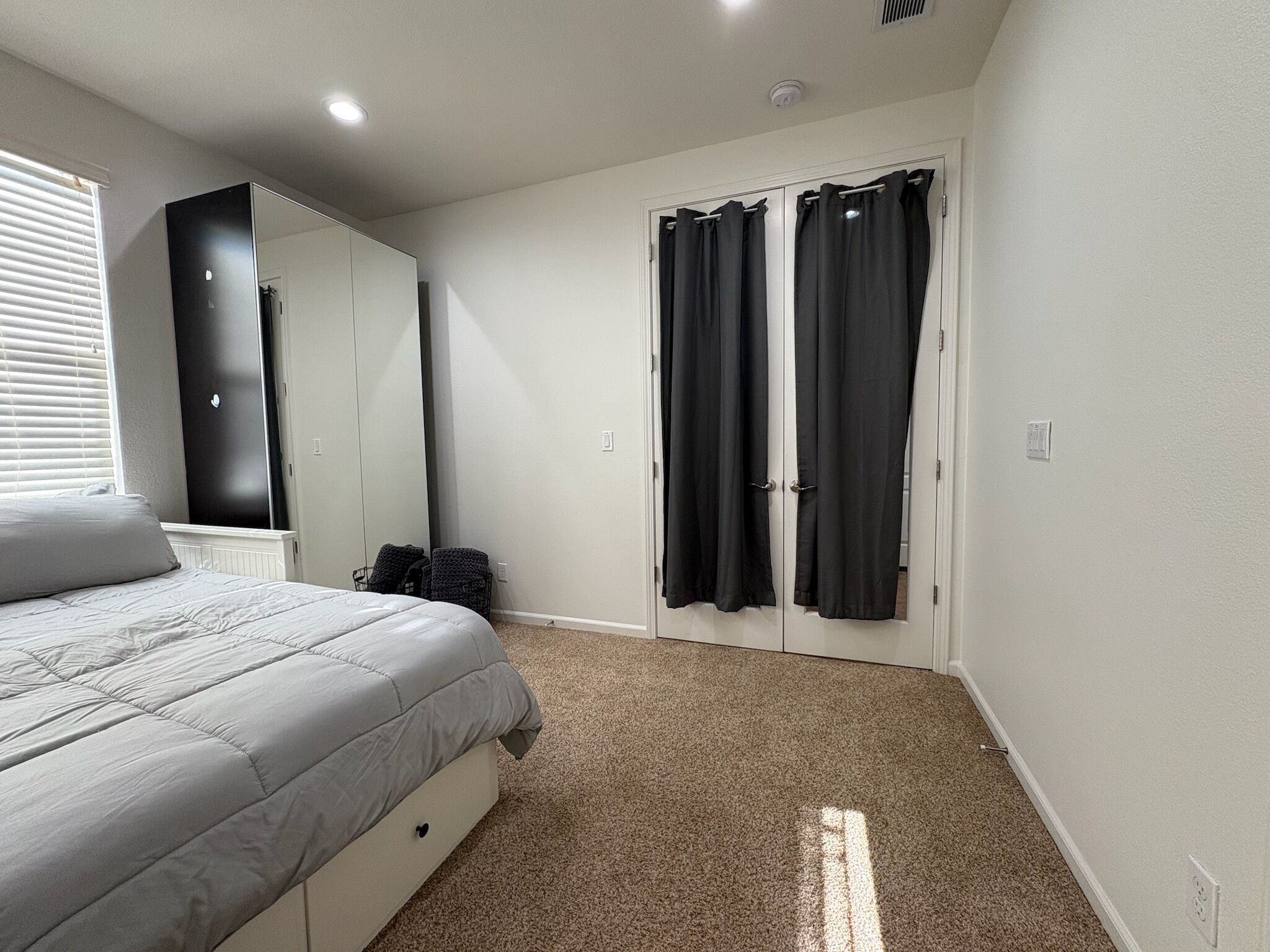 A bedroom with a bed, a wardrobe, a mirror, and a door with curtains.