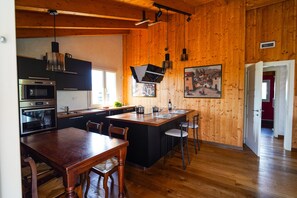 A modern kitchen with wooden walls, a central island, and a dining area with wooden furniture.