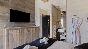 Une chambre d’hôtel moderne avec un mur en bois, un téléviseur à écran plat, un lit avec des serviettes, une salle de bain avec un lavabo et un peignoir accroché au mur.