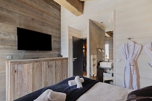 Une chambre d’hôtel moderne avec un mur en bois, un téléviseur à écran plat, un lit avec des serviettes, une salle de bain avec un lavabo et un peignoir accroché au mur.