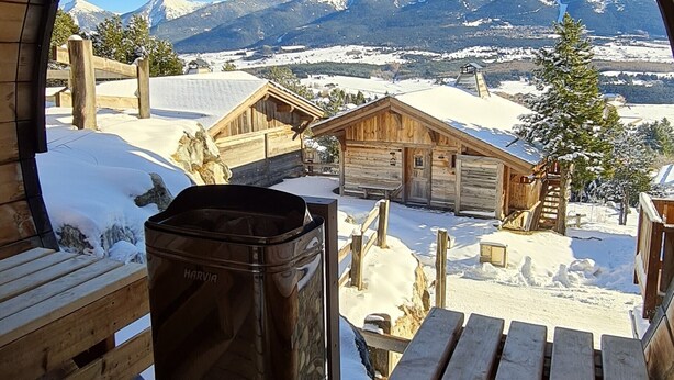 Une cabane en bois dotée d’une fenêtre circulaire donnant sur un paysage montagneux enneigé.