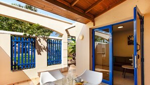 A patio with a table set for breakfast, including fruits and drinks, and a blue door leading to an indoor seating area.