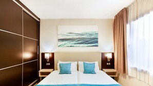 A hotel room with a large bed, two bedside tables with lamps, a wall-mounted artwork, and a window with curtains.