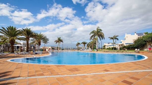 A large outdoor swimming pool with a tiled deck, surrounded by palm trees and lounge chairs.