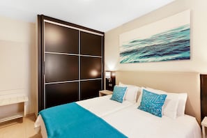 Une chambre d’hôtel avec un grand lit, une armoire noire, une œuvre d’art accrochée au mur et une table de chevet avec une lampe.