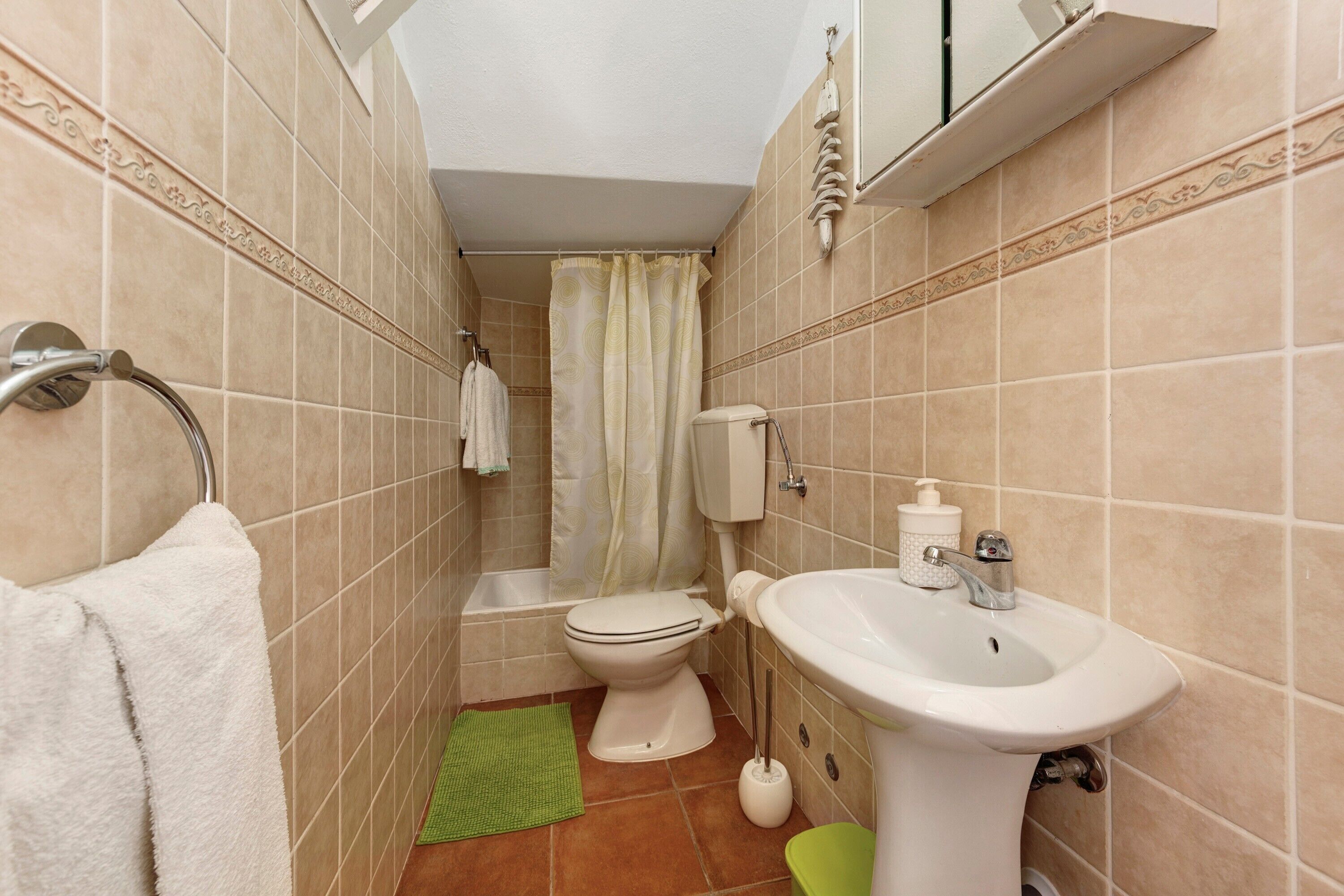 A bathroom with a toilet, sink, shower curtain, and a green mat.