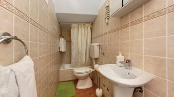 A bathroom with a toilet, sink, shower curtain, and a green mat.
