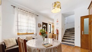 A dining area with a round table, chairs, a vase with flowers, a book, and a staircase in the background. - Holiday Home 'Acolhedora' with Private Garden, Wi-Fi and Air Conditioning (Lagos)