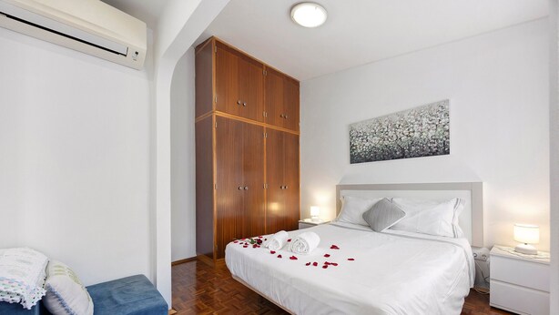 A hotel room with a bed, a wardrobe, a bedside table, and a wall-mounted artwork. - Holiday Home 'Acolhedora' with Private Garden, Wi-Fi and Air Conditioning (Lagos)