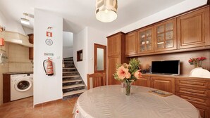 A kitchen with wooden cabinets, a washing machine, a dining table with a tablecloth, and a fire extinguisher on the wall. - Holiday Home 'Acolhedora' with Private Garden, Wi-Fi and Air Conditioning (Lagos)