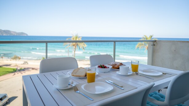 A table set for breakfast with a view of the ocean and beach. - Apartment 'Sa Maniga' with Sea View, Wi-Fi and Air Conditioning (Sant Llorenç des Cardassar)