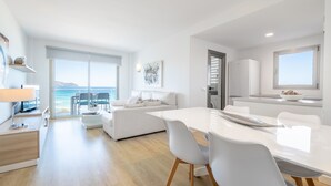 A modern kitchen with white appliances, a dining area with a white table and chairs, and a view of the sea through large windows. - Apartment 'Sa Maniga' with Sea View, Wi-Fi and Air Conditioning (Sant Llorenç des Cardassar)