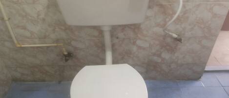 Un inodoro con tanque y asiento blancos, frente a una pared con diseño de mármol, sobre un suelo azul.