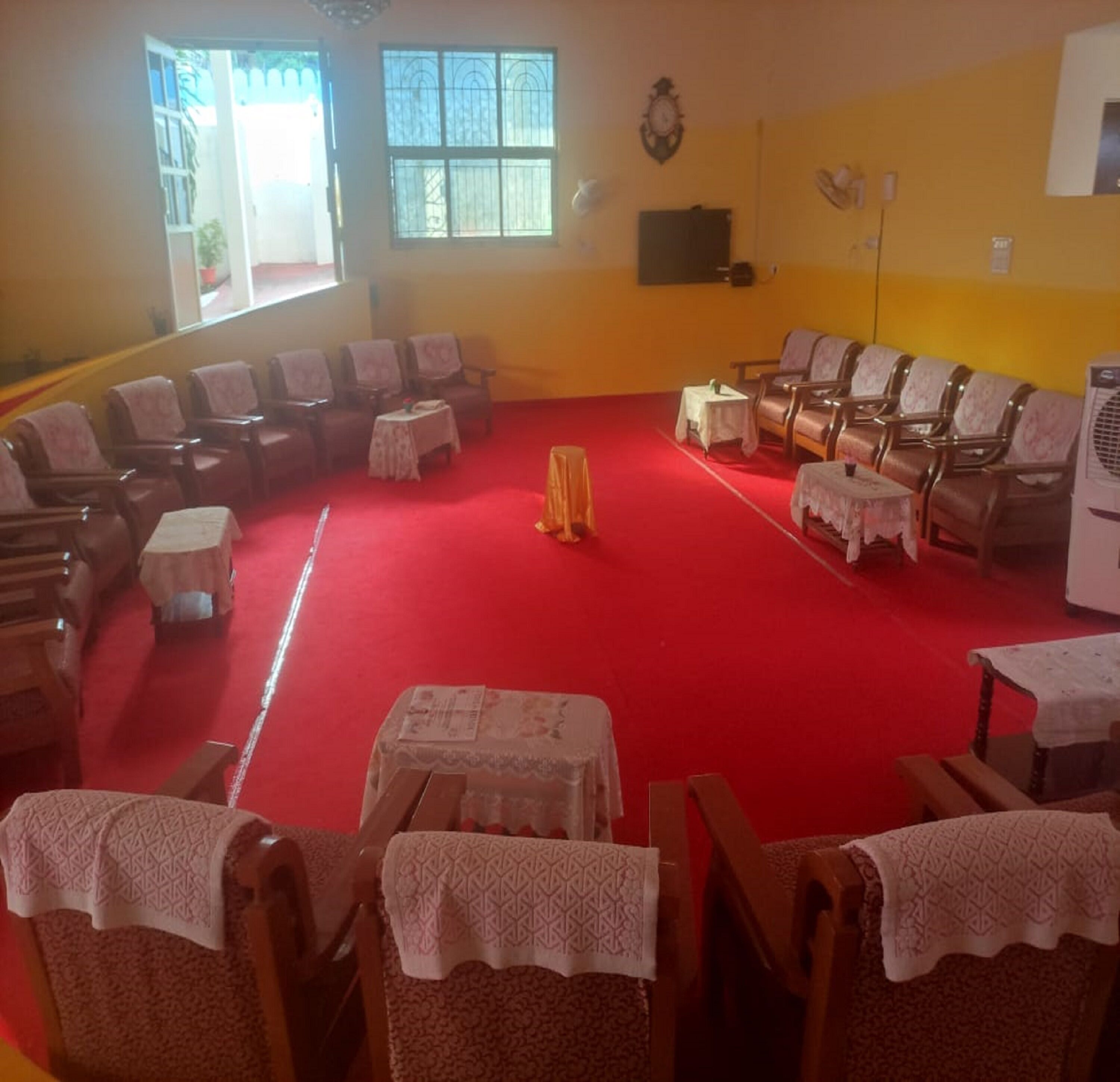 A room with a red carpet, wooden chairs, and tables with white tablecloths.