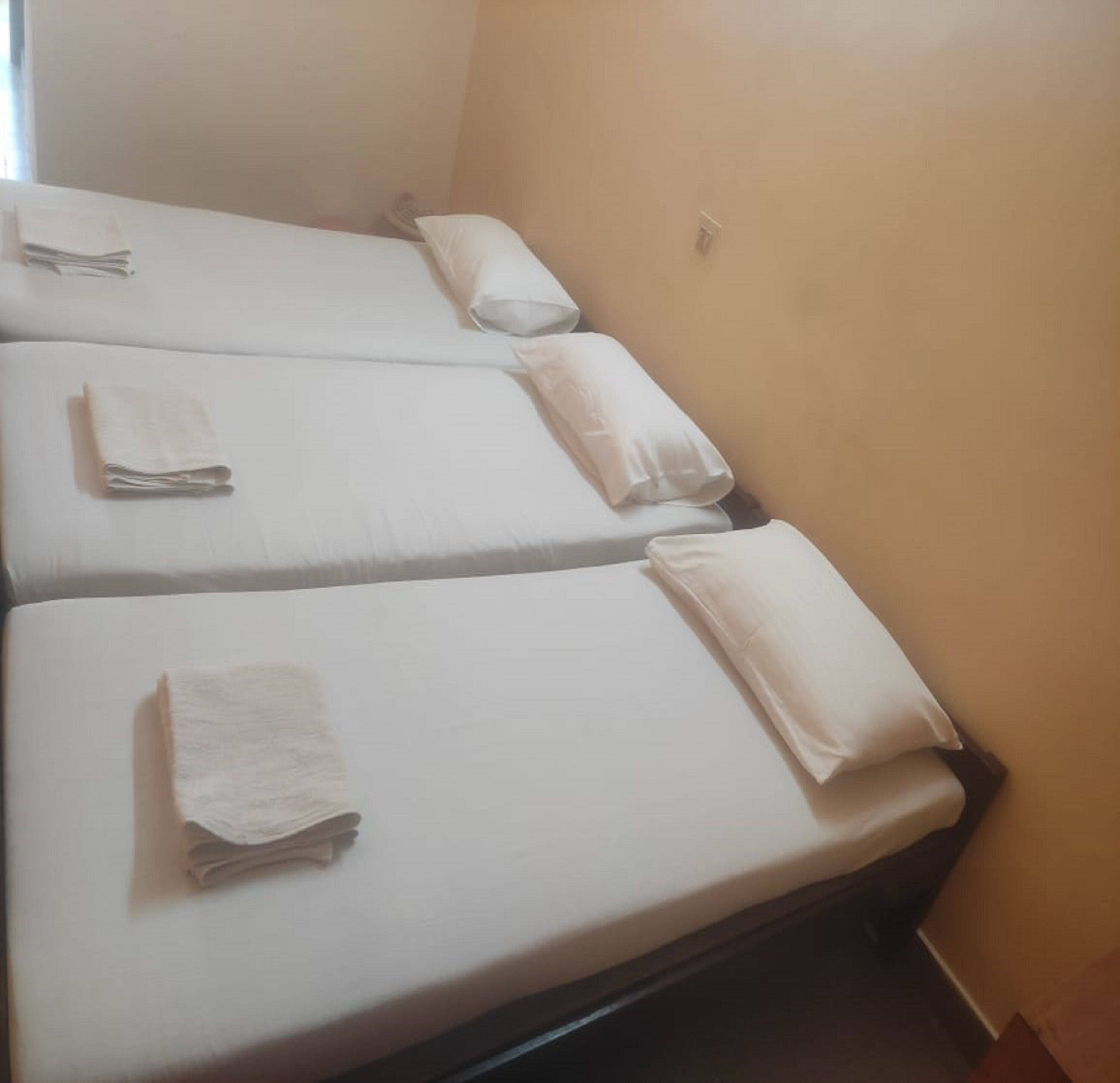 A room with three single beds, each with a neatly folded white towel.