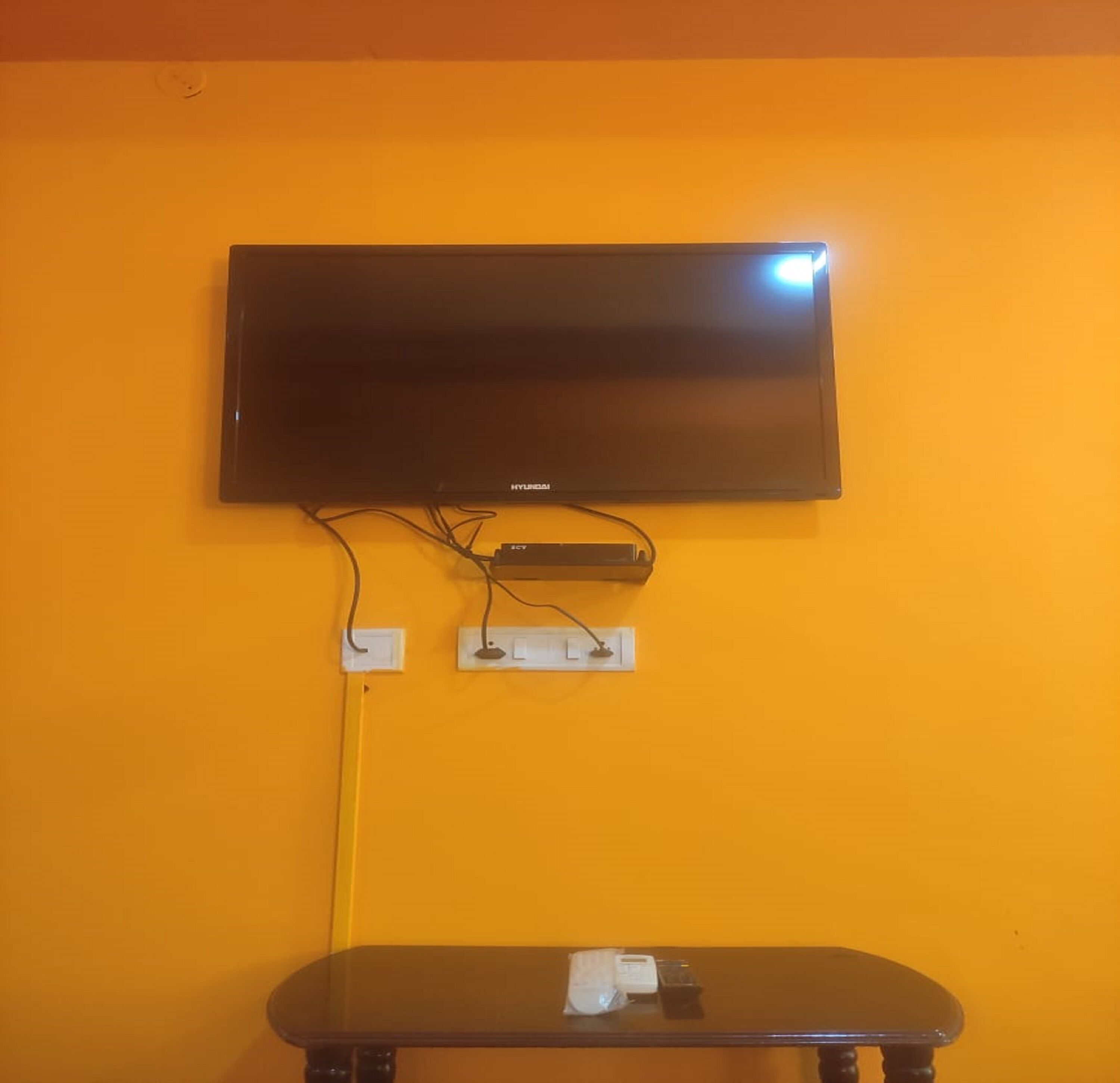 A flat-screen TV mounted on a yellow wall with a power strip below it.