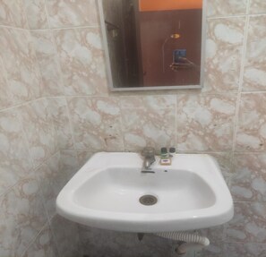 A bathroom with a white sink, a mirror above it, and a tiled wall. - Hotel St Thomas International Centre (Chennai)