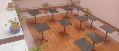 A rooftop terrace with multiple square tables and potted plants.