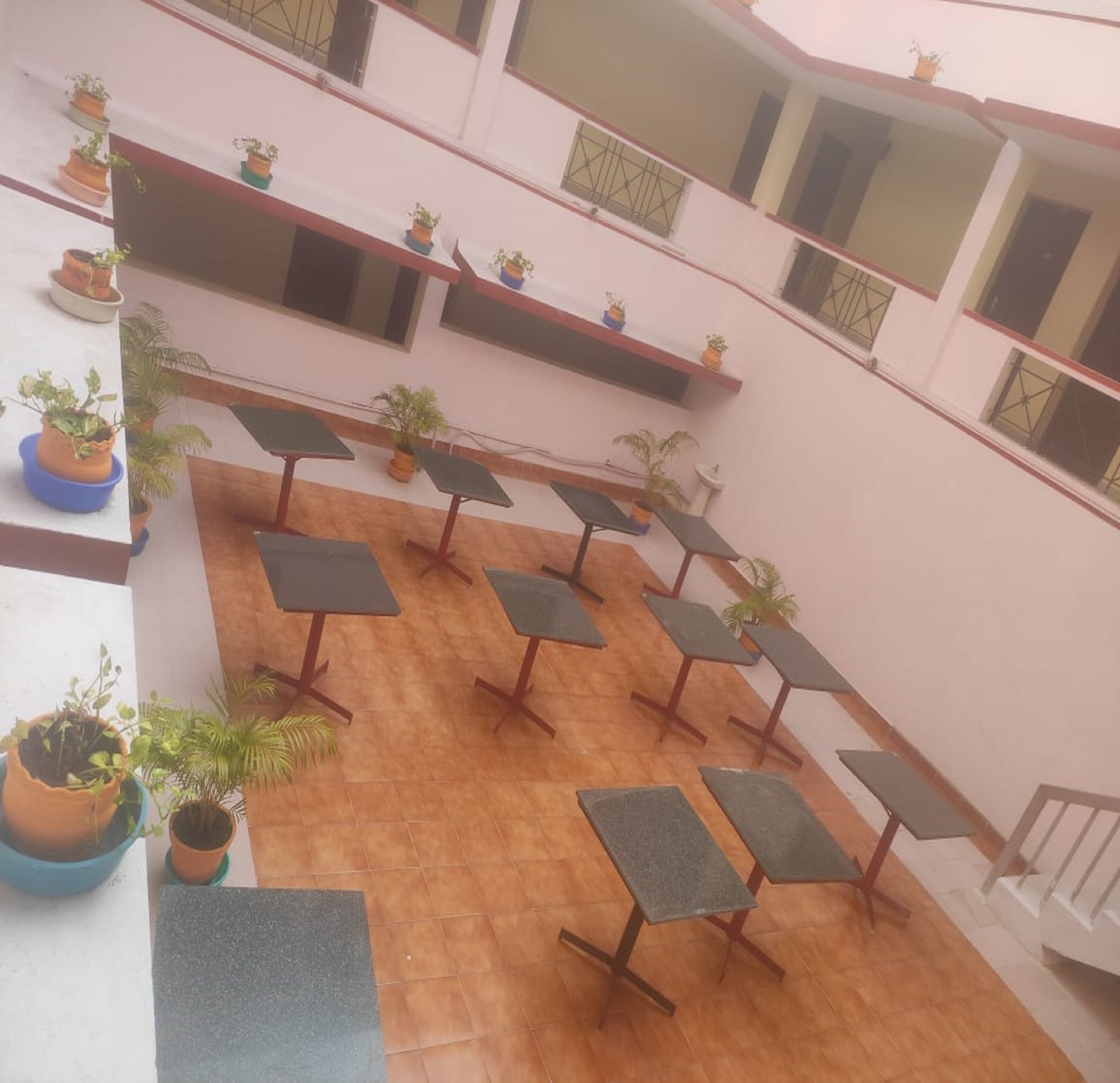 Een binnenplaats met meerdere tafels en potplanten, omringd door een wit gebouw met balkons.