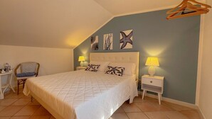 A bedroom with a bed, two bedside tables, a chair, and wall art. - 49 Sea Rooms - Blue Room (Stintino)