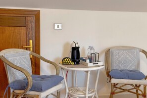 Une pièce comprenant deux fauteuils en osier, une petite table avec une machine à café et une porte.