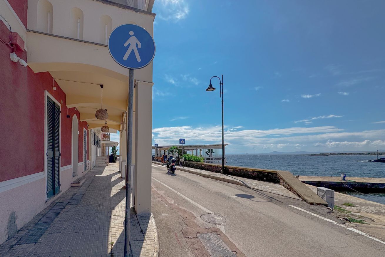 A coastal street with a pedestrian sign, a motorcyclist, and a building with a red facade.