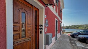 A red building with a wooden door, a sign indicating '49 SEA ROOMS,' and a view of the sea.