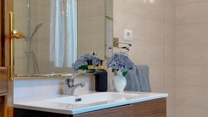 A bathroom with a white sink, a mirror, a shower, and two vases with flowers.
