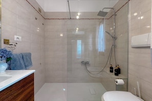 Ein modernes Badezimmer mit einer Duschkabine aus Glas, einer Toilette, einem Waschbecken mit Holzschrank und einem Handtuchhalter.