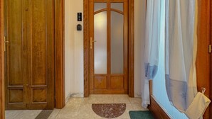 A wooden door with a glass panel, a number plaque, and a mat on the floor.