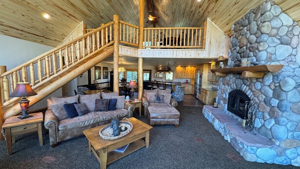 A spacious living area with a wooden staircase, a stone fireplace, and a cozy seating arrangement. - PICKLEBALL Paradise! HotTub/Huge GameRoom/Mtn views/Fido Friendly/best location! (Grand Lake)