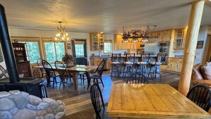 A spacious kitchen with wooden cabinets, a stone accent wall, and a dining area with a large wooden table and chairs. - PICKLEBALL Paradise! HotTub/Huge GameRoom/Mtn views/Fido Friendly/best location! (Grand Lake)