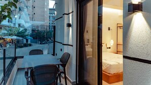 A balcony with a table and chairs, a bed with a wooden headboard, and a view of the cityscape. - Gloal Suites Residence (Sarande)