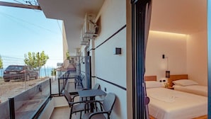 A balcony with a table and chairs, a bed with a nightstand, and a view of the sea. - Gloal Suites Residence (Sarande)