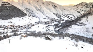 Un pueblo cubierto de nieve en la montaña, con edificios tradicionales y una pista de esquí.